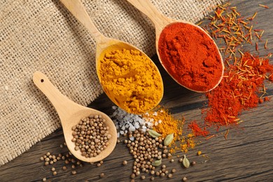 Photo of Different aromatic spices in spoons on wooden table, flat lay