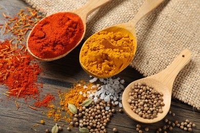 Photo of Different aromatic spices in spoons on wooden table, closeup