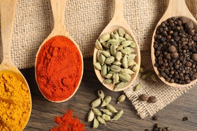 Photo of Different aromatic spices in spoons on wooden table, flat lay