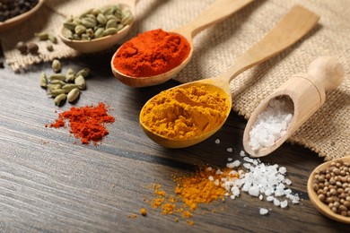 Photo of Different aromatic spices in spoons and scoop on wooden table, closeup