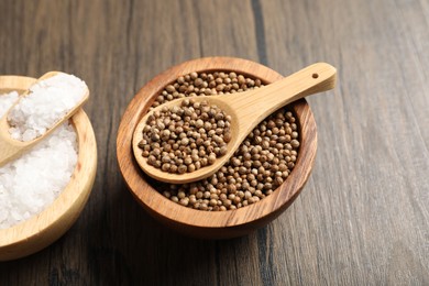 Photo of Aromatic spices. Coriander seeds and salt on wooden table, closeup
