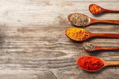 Photo of Different aromatic spices in spoons on wooden table, closeup. Space for text