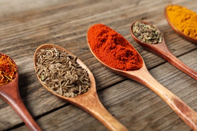 Photo of Different aromatic spices in spoons on wooden table, closeup