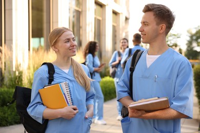 Photo of Medical students in uniforms with notebooks near building outdoors, selective focus