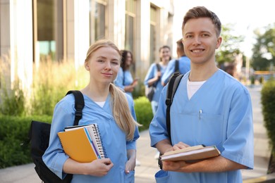 Photo of Medical students in uniforms with notebooks near building outdoors, selective focus
