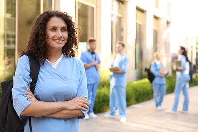 Photo of Happy medical student in uniform with backpack near building outdoors, selective focus