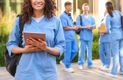Photo of Medical student in uniform with backpack and tablet near building outdoors, selective focus