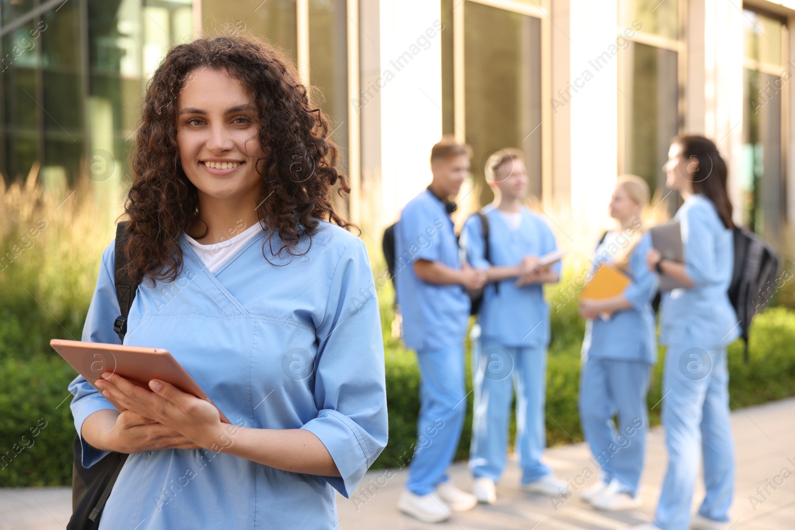 Photo of Happy medical student in uniform with backpack and tablet near building outdoors, selective focus