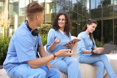 Photo of Group of medical students in uniforms studying together near building outdoors