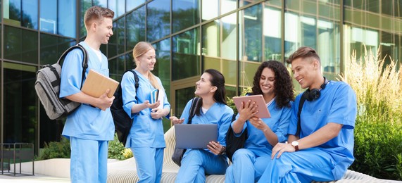 Photo of Group of medical students in uniforms studying together near building outdoors
