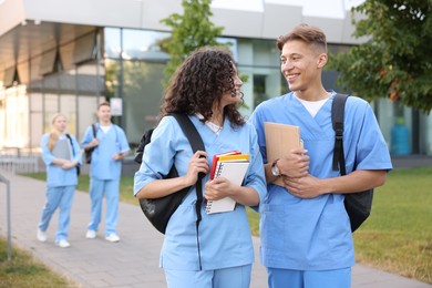 Photo of Medical students in uniforms with backpacks and notebooks outdoors, selective focus