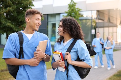 Photo of Medical students in uniforms with backpacks and notebooks outdoors, selective focus