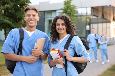 Photo of Medical students in uniforms with backpacks and notebooks outdoors, selective focus