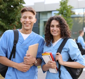 Photo of Medical students in uniforms with backpacks and notebooks outdoors