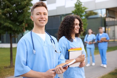 Photo of Medical students in uniforms with notebooks outdoors, selective focus