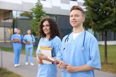 Photo of Medical students in uniforms with notebooks outdoors, selective focus