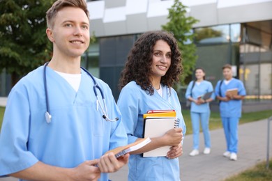 Photo of Medical students in uniforms with notebooks outdoors, selective focus