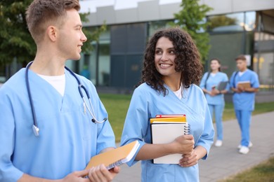 Photo of Medical students in uniforms with notebooks outdoors, selective focus