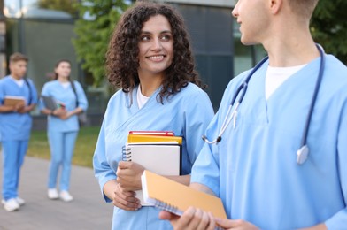 Photo of Medical students in uniforms with notebooks outdoors, selective focus