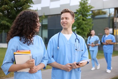 Photo of Medical students in uniforms with notebooks outdoors, selective focus