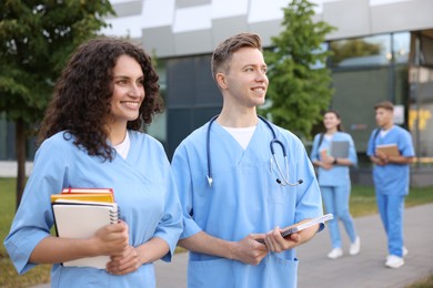 Photo of Medical students in uniforms with notebooks outdoors, selective focus