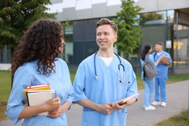 Photo of Medical students in uniforms with notebooks outdoors, selective focus