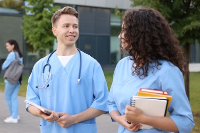 Photo of Medical students in uniforms with notebooks outdoors, selective focus
