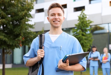 Photo of Medical student in uniform with backpack, laptop and notebook outdoors, selective focus