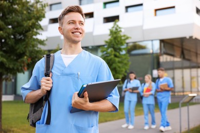 Photo of Medical student in uniform with backpack, laptop and notebook outdoors, selective focus