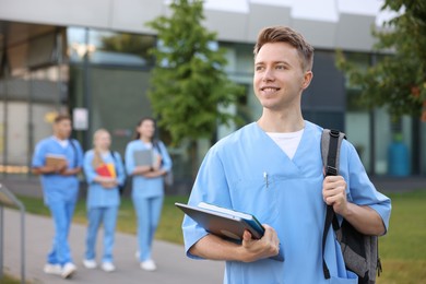 Photo of Medical student in uniform with backpack, laptop and notebook outdoors, selective focus