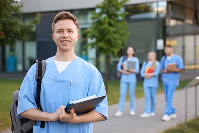 Photo of Medical student in uniform with backpack, laptop and notebook outdoors, selective focus