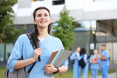 Photo of Medical student in uniform with backpack and notebooks outdoors, selective focus