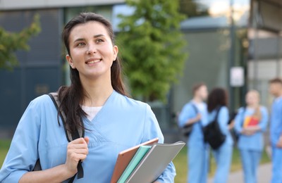 Photo of Medical student in uniform with backpack and notebooks outdoors, selective focus
