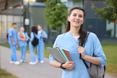 Photo of Medical student in uniform with backpack and notebooks outdoors, selective focus