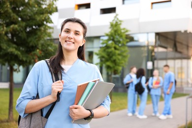 Photo of Medical student in uniform with backpack and notebooks outdoors, selective focus