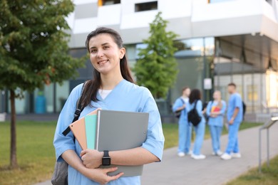 Photo of Medical student in uniform with backpack and notebooks outdoors, selective focus
