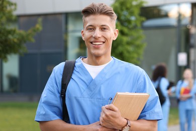 Photo of Medical student in uniform with backpack and notebook outdoors, selective focus