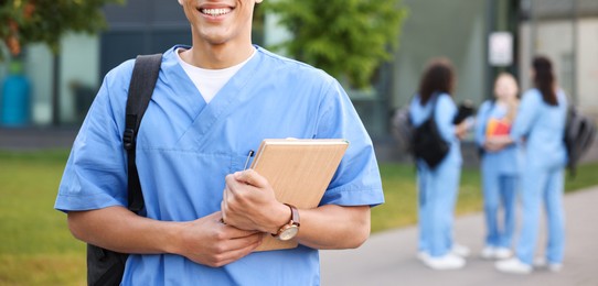 Photo of Medical student in uniform with backpack and notebook outdoors, selective focus