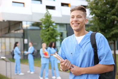 Photo of Medical student in uniform with backpack and notebooks outdoors, selective focus