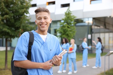 Photo of Medical student in uniform with backpack and notebooks outdoors, selective focus