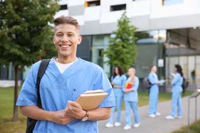 Photo of Medical student in uniform with backpack and notebooks outdoors, selective focus