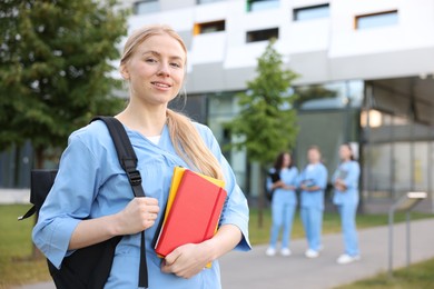 Photo of Medical student in uniform with backpack and notebooks outdoors, selective focus