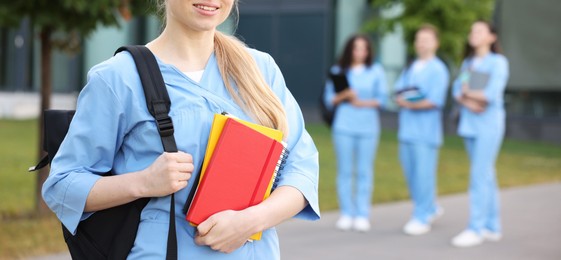 Photo of Medical student in uniform with backpack and notebooks outdoors, selective focus