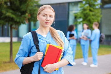 Photo of Medical student in uniform with backpack and notebooks outdoors, selective focus