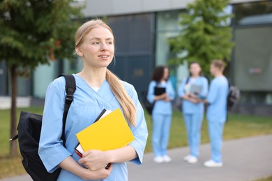 Photo of Medical student in uniform with backpack and notebooks outdoors, selective focus