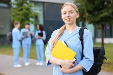 Photo of Medical student in uniform with backpack and notebooks outdoors, selective focus
