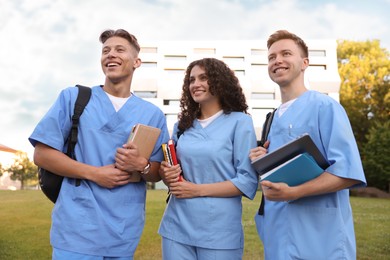 Photo of Medical students in uniforms with backpacks and notebooks outdoors
