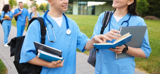 Photo of Medical students in uniforms with backpacks and notebooks outdoors, selective focus