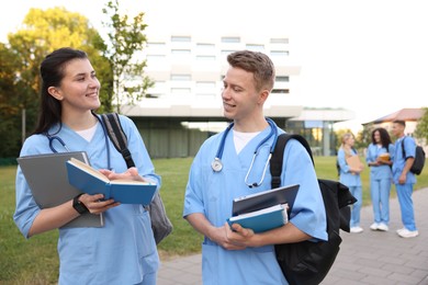 Photo of Medical students in uniforms with backpacks and notebooks outdoors, selective focus