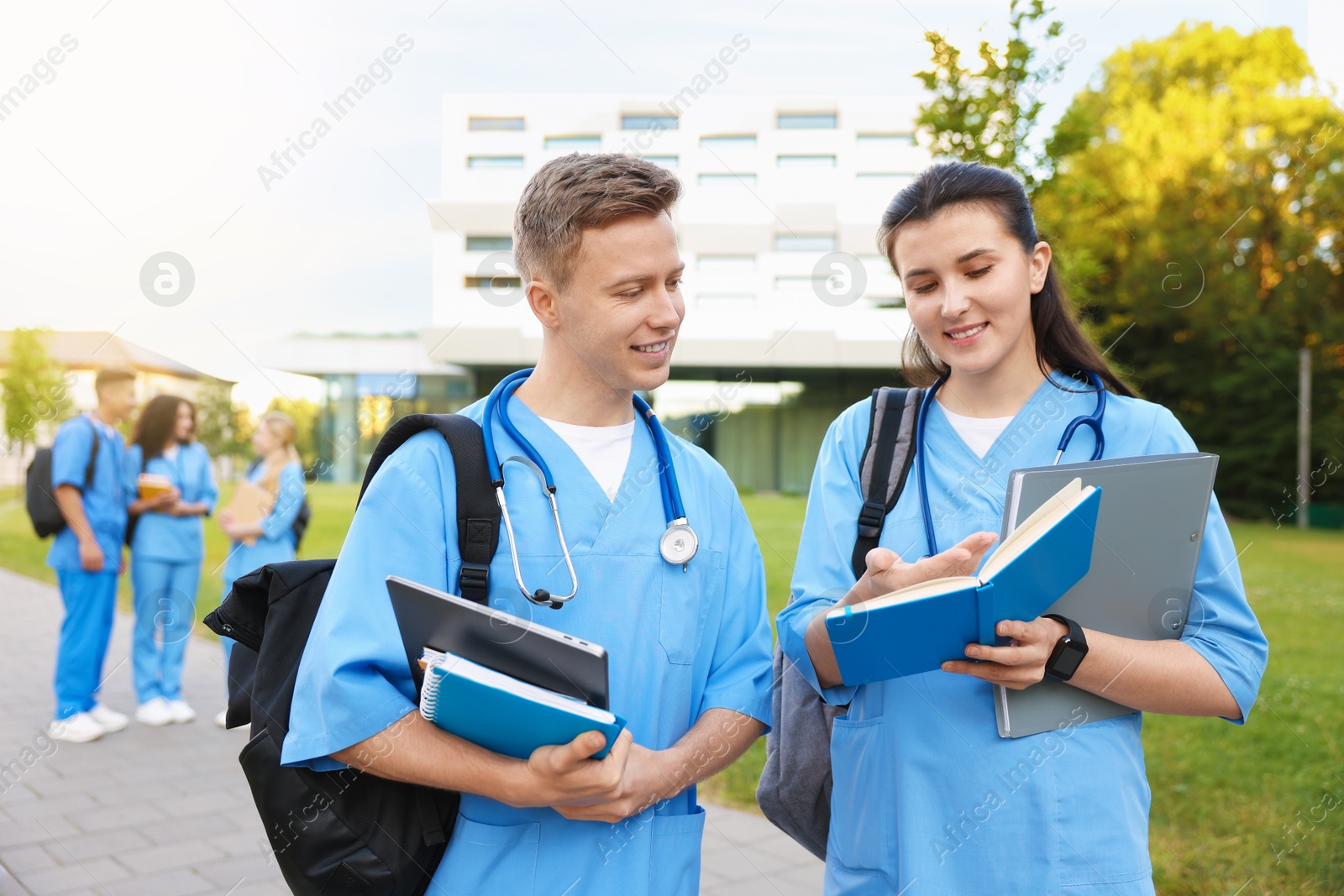 Medical students in uniforms with backpacks and notebooks outdoors, selective focus Photo of Medical students in uniforms with backpacks and notebooks outdoors, selective focus
